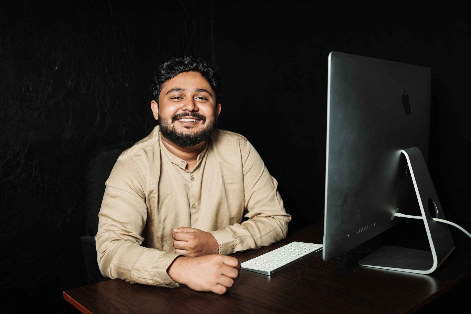 Un jeune professionnel souriant, assis à un bureau devant un ordinateur dans un bureau lumineux.
