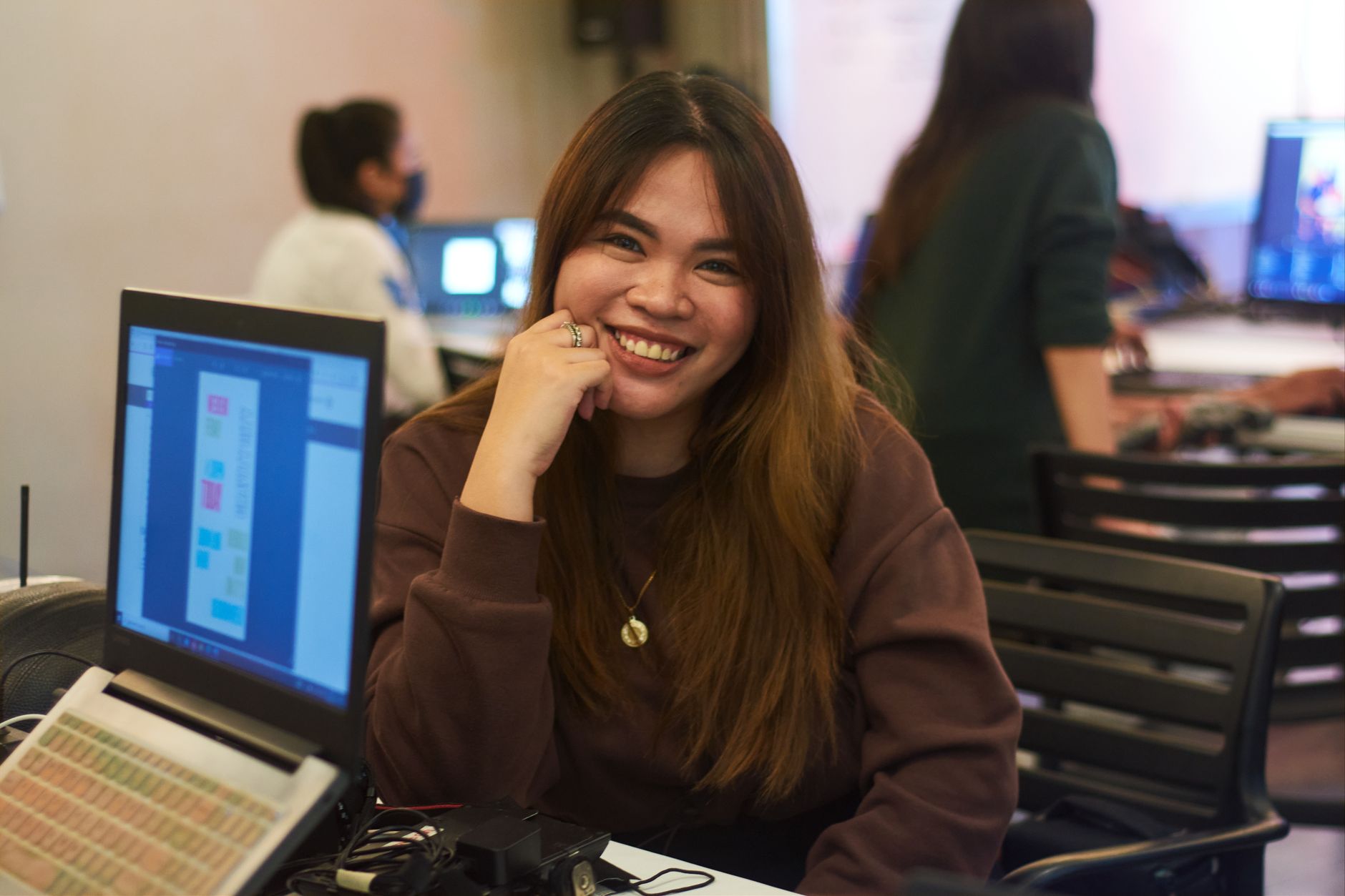 Une professionnelle souriante qui travaille à son bureau avec des ordinateurs portables dans un environnement de bureau animé.