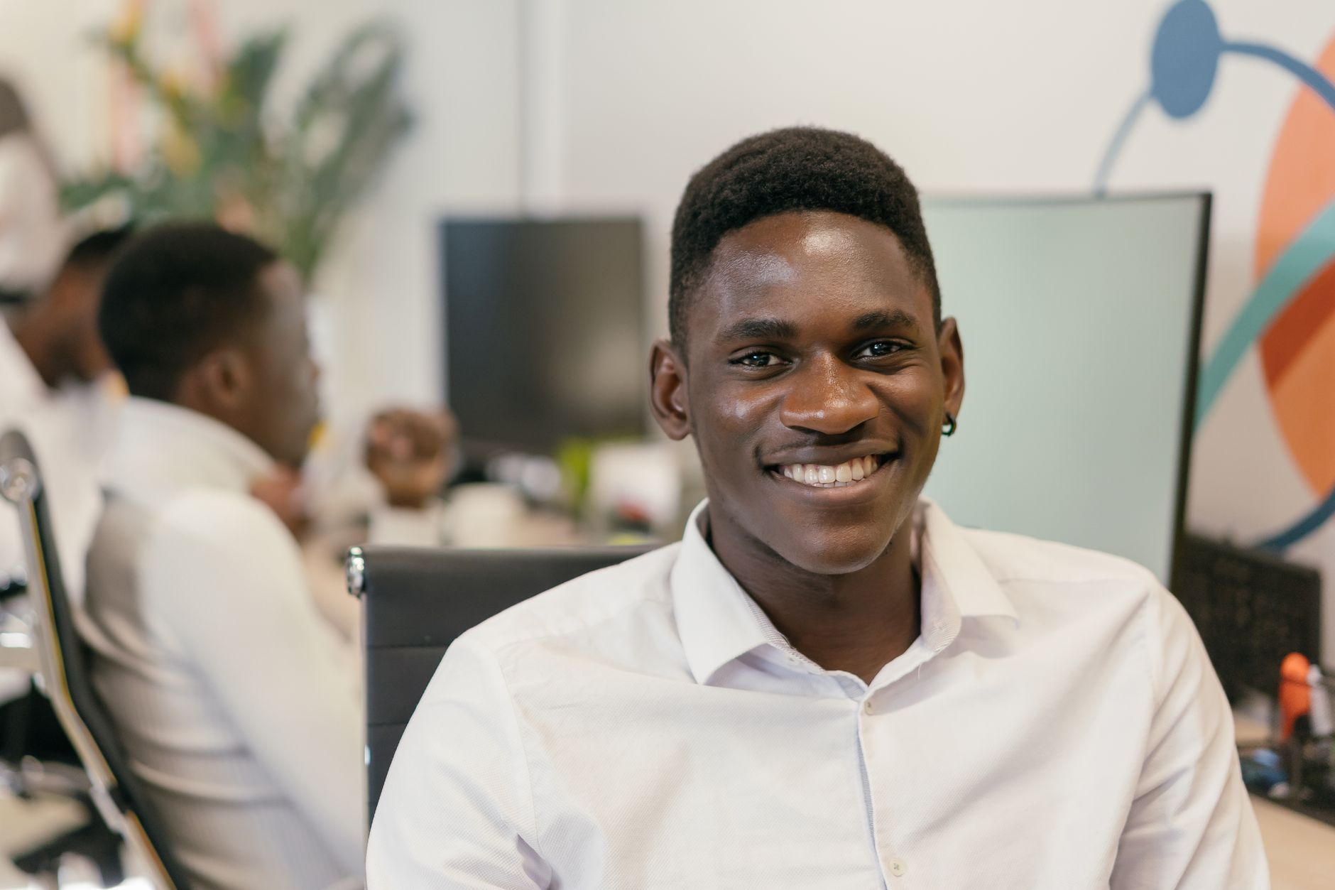 Un jeune homme souriant à son bureau dans un environnement de bureau moderne.